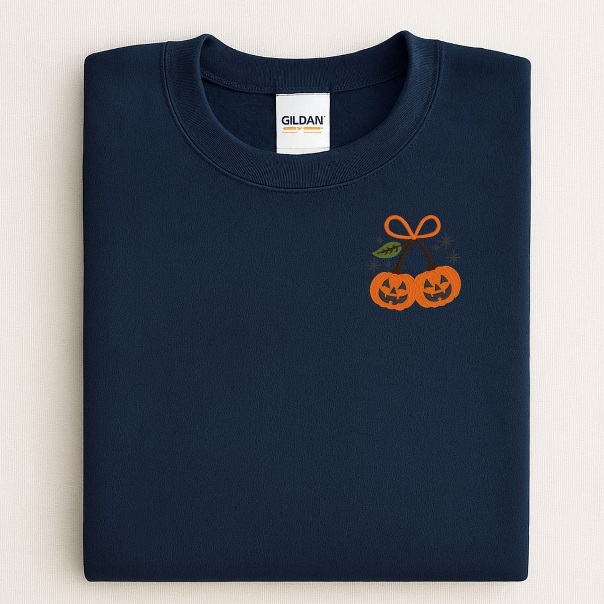 Folded Navy Gildan crewneck with two orange embroidered jack-o-lanterns