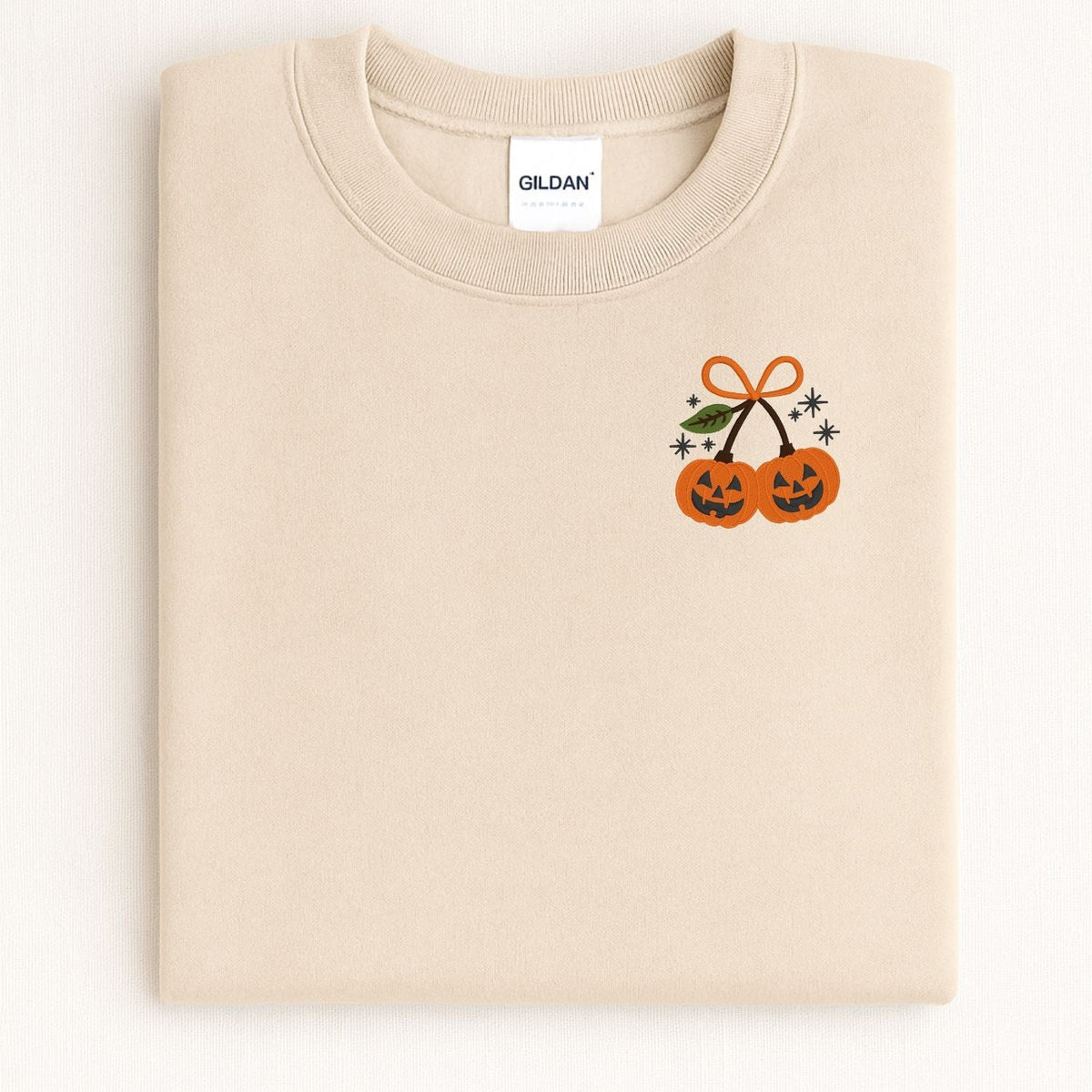 Folded Sand Gildan sweatshirt showing the embroidered pumpkin pair design