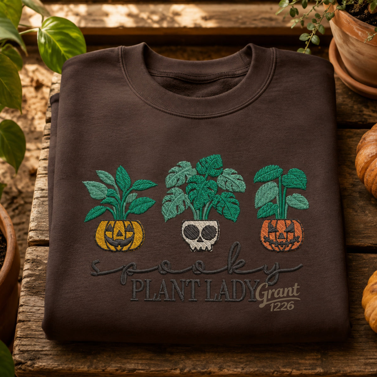 Chocolate embroidered Spooky Plant Lady Gildan crewneck sweatshirt shown with pumpkins and houseplants.