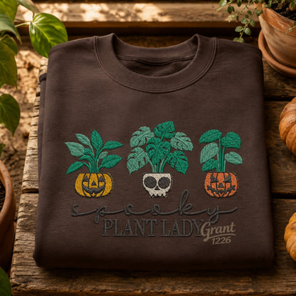 Chocolate embroidered Spooky Plant Lady Gildan crewneck sweatshirt shown with pumpkins and houseplants.
