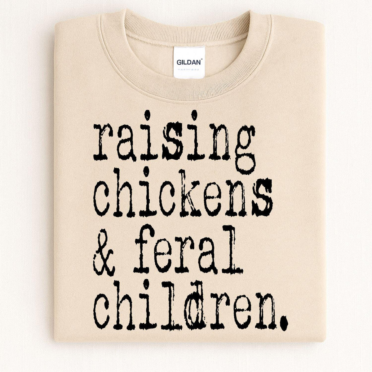 Folded sand crewneck with Raising Chickens and Feral Children graphic
