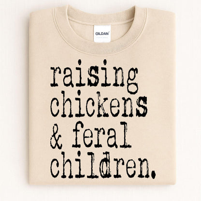 Folded sand crewneck with Raising Chickens and Feral Children graphic