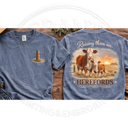 Blue t-shirt with cow design and 'Raising them an Herefords' text on a wooden surface
