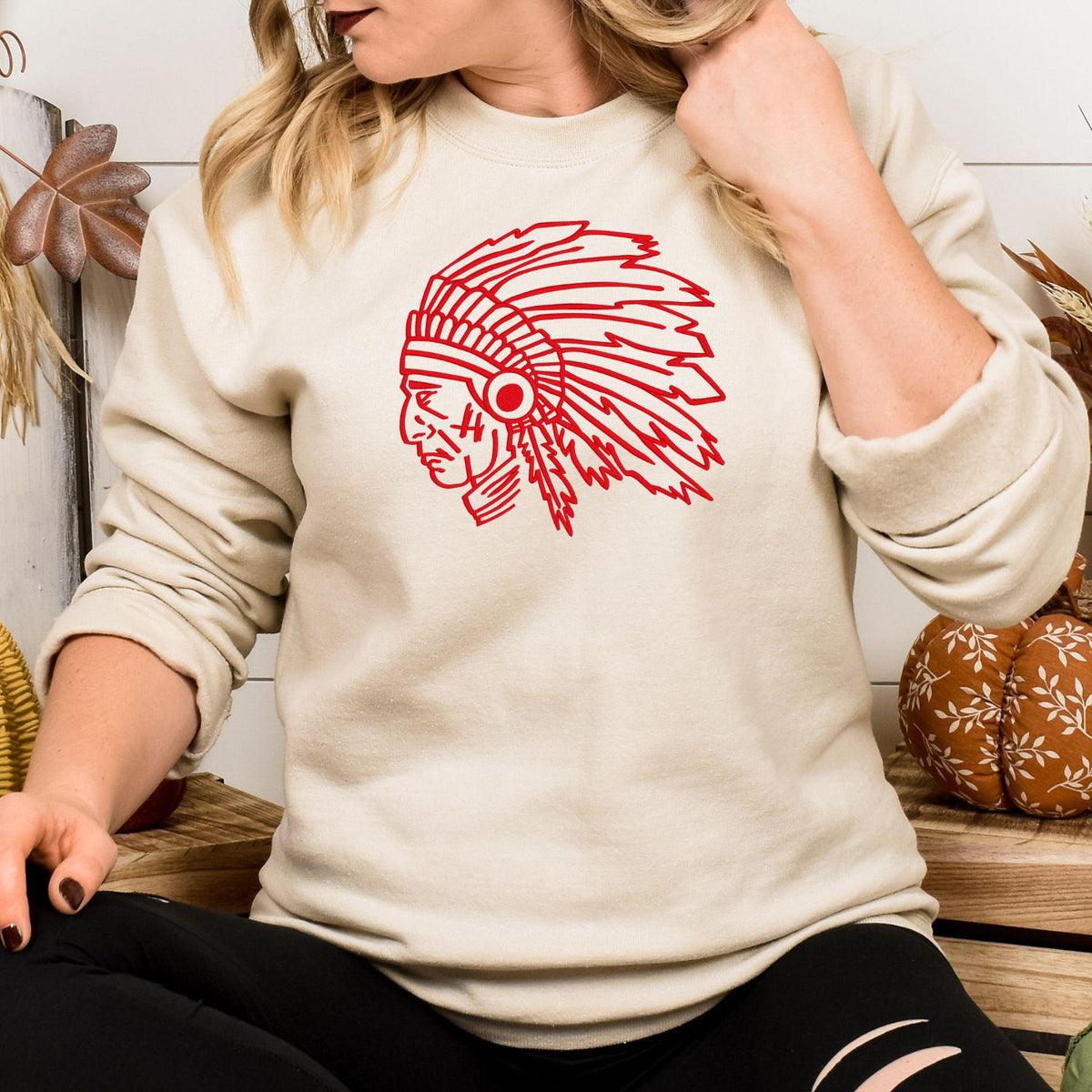 Sand crewneck with a red embroidered headdress mascot modeled indoors