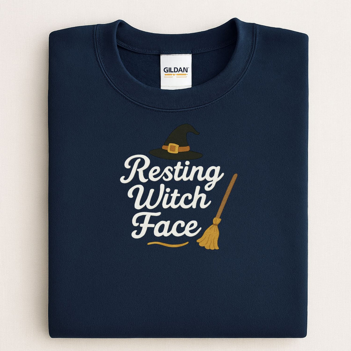 Folded Navy Gildan sweatshirt with Resting Witch Face witch hat and broom embroidery