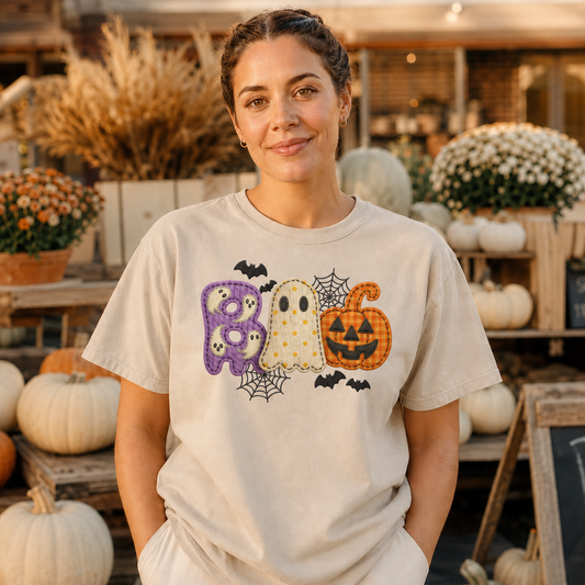 Adult wearing Sandstone Comfort Colors BOO Halloween shirt with purple ghost letter, cream ghost, orange pumpkin, bats and webs