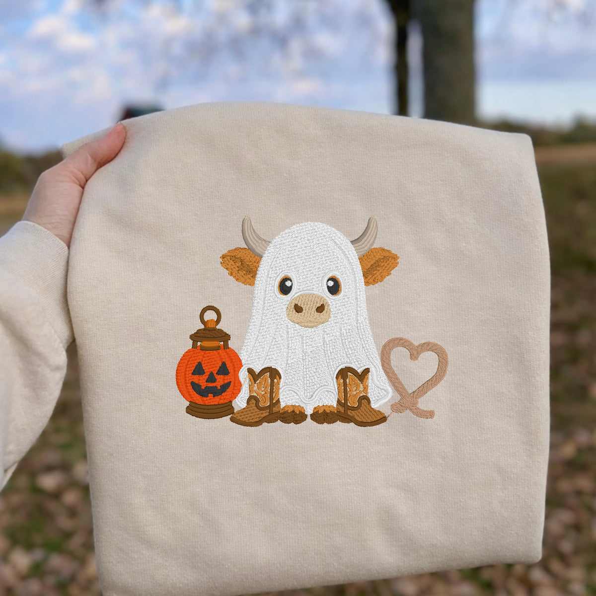 Close-up of ghost cow and pumpkin pail embroidery on a Sand sweatshirt