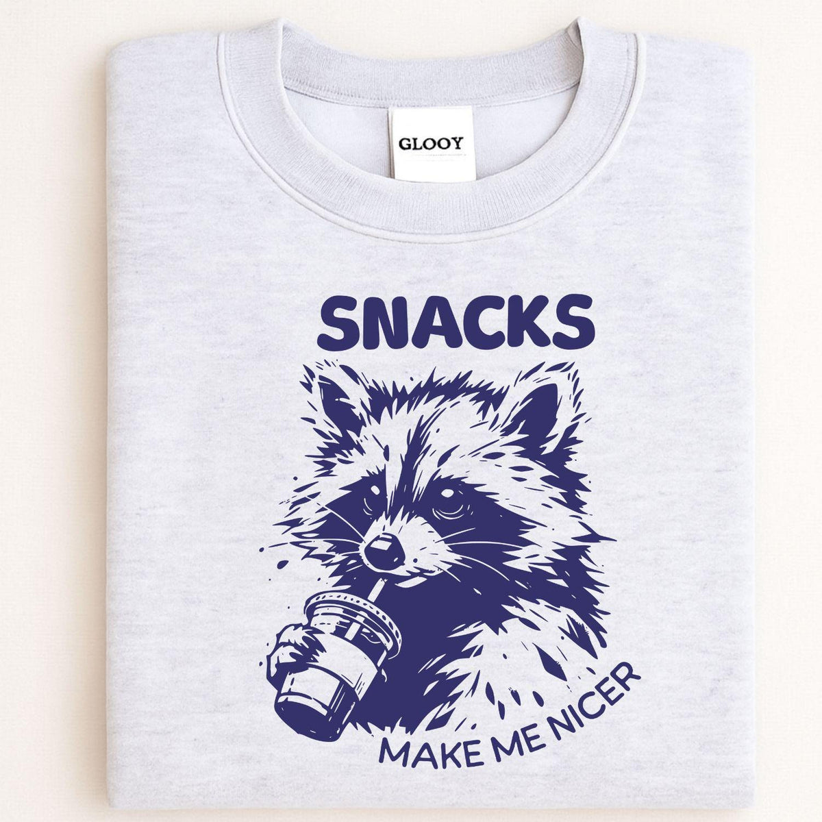Folded ash gray crewneck with Snacks Make Me Nicer raccoon design