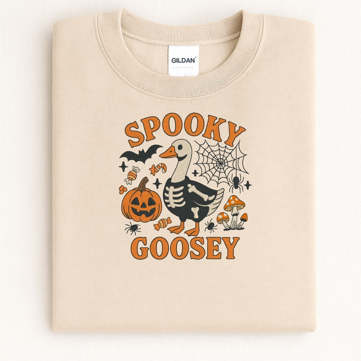 Folded sand sweatshirt showing the skeleton goose, jack-o-lantern and mushroom embroidery