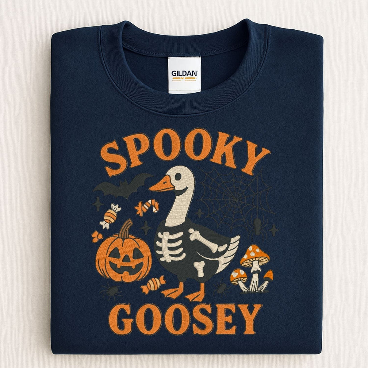 Folded navy Gildan sweatshirt with Spooky Goosey skeleton goose Halloween embroidery