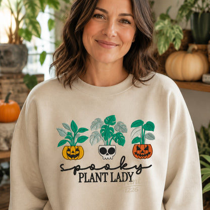 Smiling model wearing sand Spooky Plant Lady embroidered sweatshirt in a greenhouse