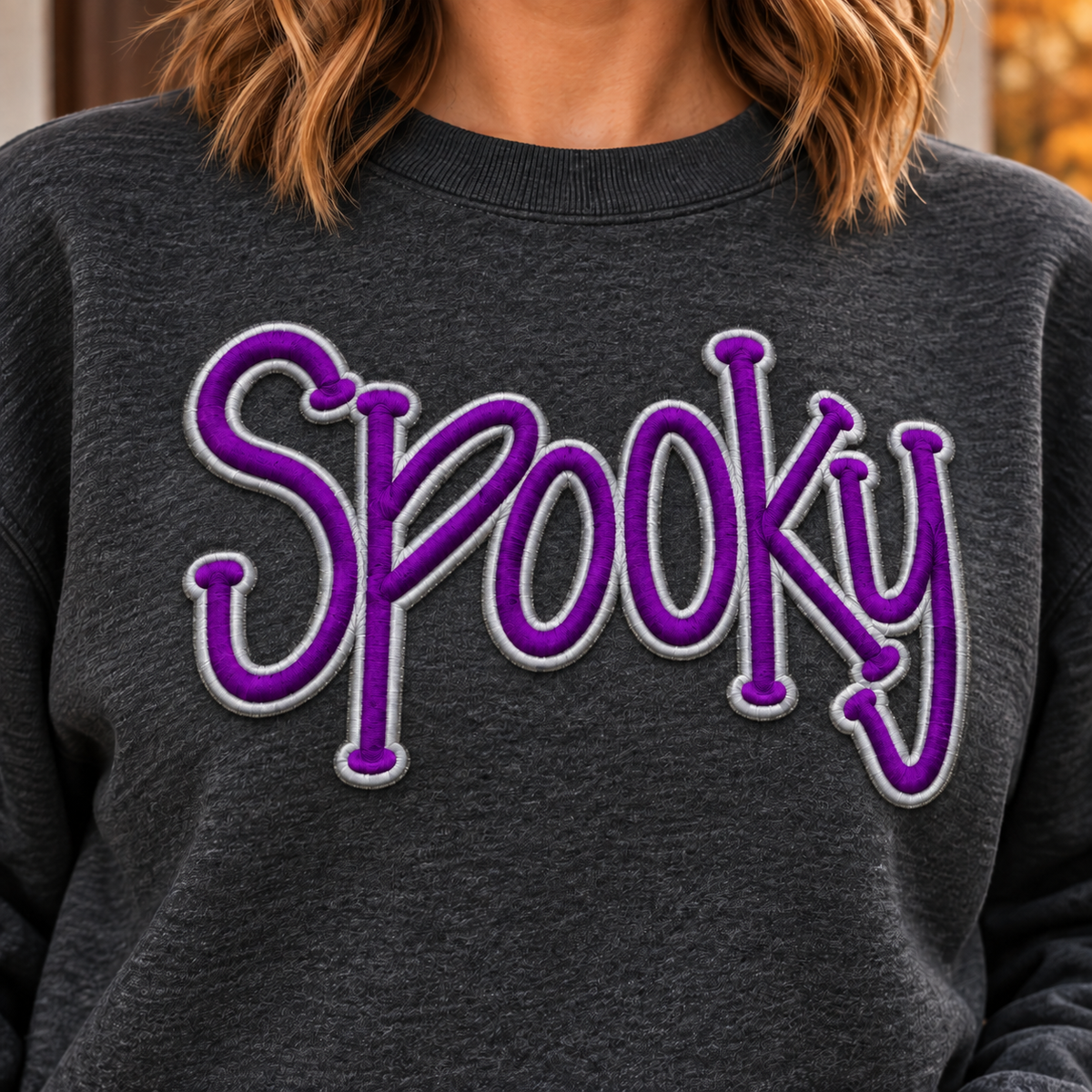 Close-up of raised purple and silver Spooky puff embroidery on a heather black sweatshirt