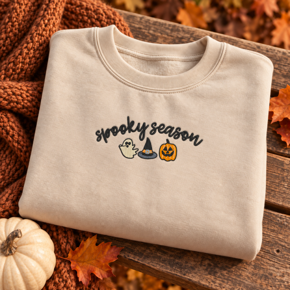 Folded sand sweatshirt featuring the 8 by 3 inch Spooky Season embroidery