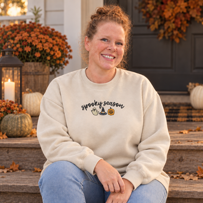 Woman seated in a sand sweatshirt with a compact Spooky Season embroidered design