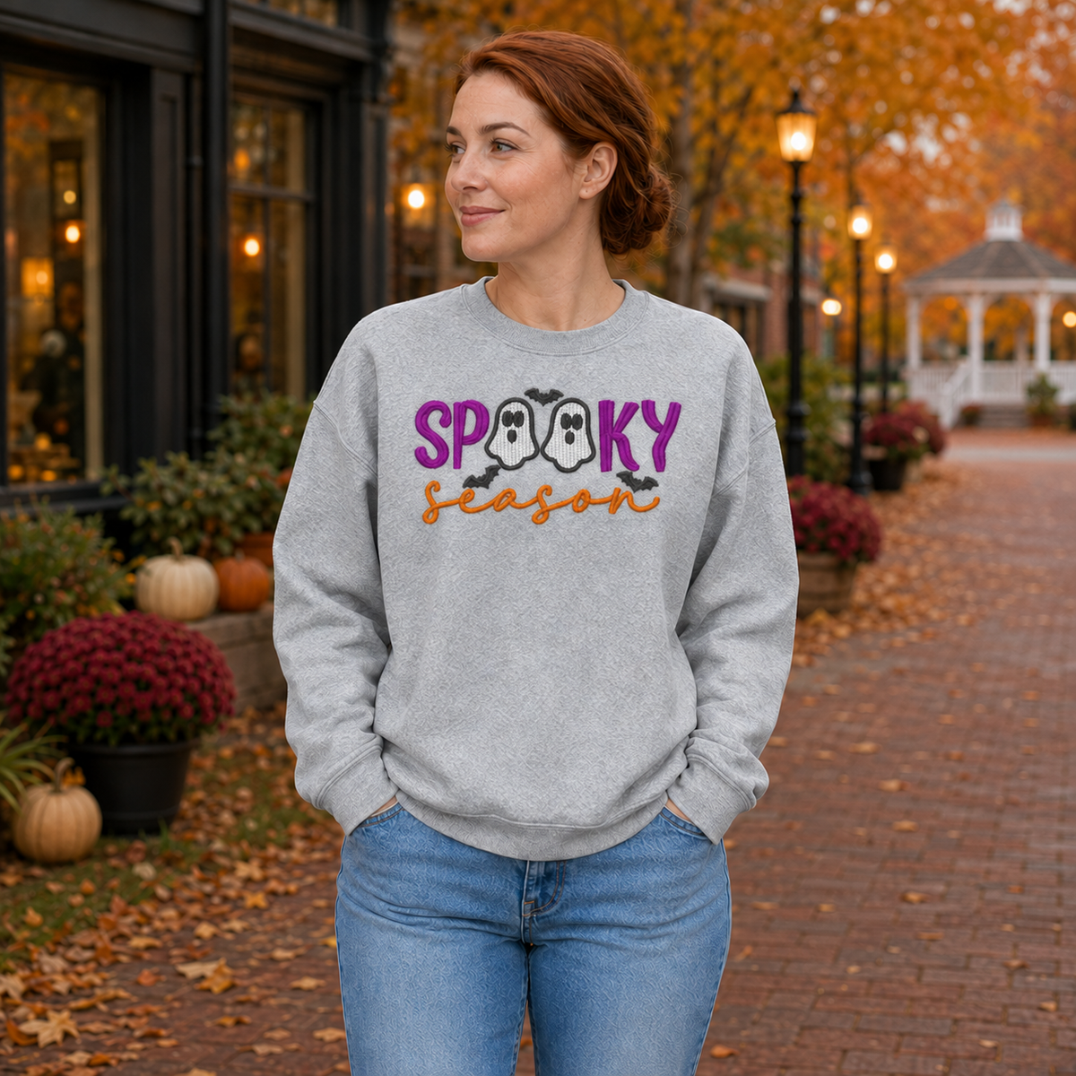 Woman wearing a Spooky Season ghost embroidered Sport Grey sweatshirt in an autumn town