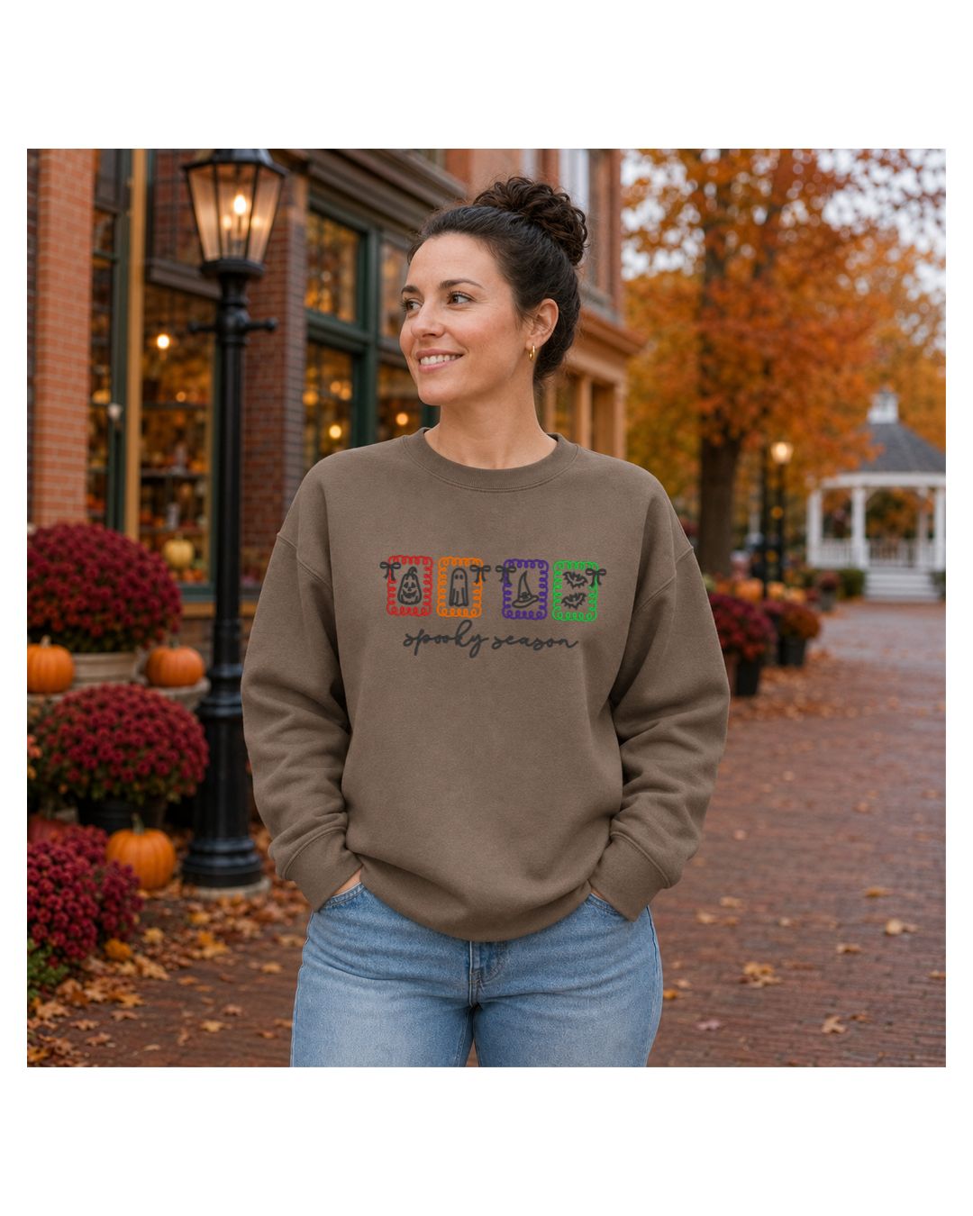 Woman wearing a neutral crewneck sweatshirt embroidered with Spooky Season Halloween icons outdoors in fall