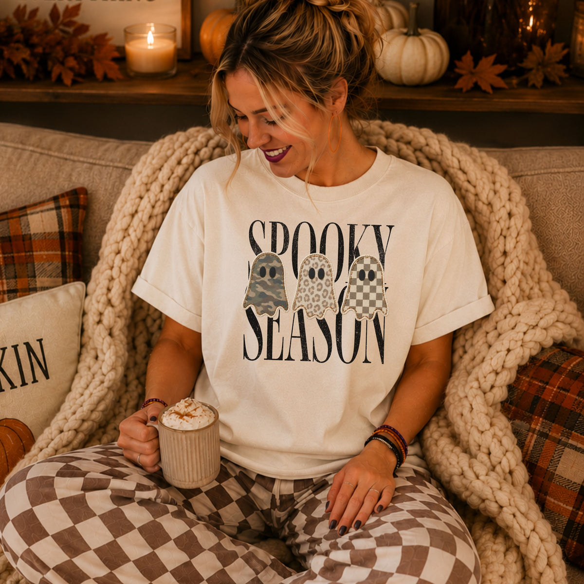 Woman wearing a white Spooky Season patchwork ghost DTG T-shirt in a cozy autumn setting