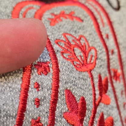Close-up of coral floral pumpkin embroidery stitching on a Sport Grey sweatshirt