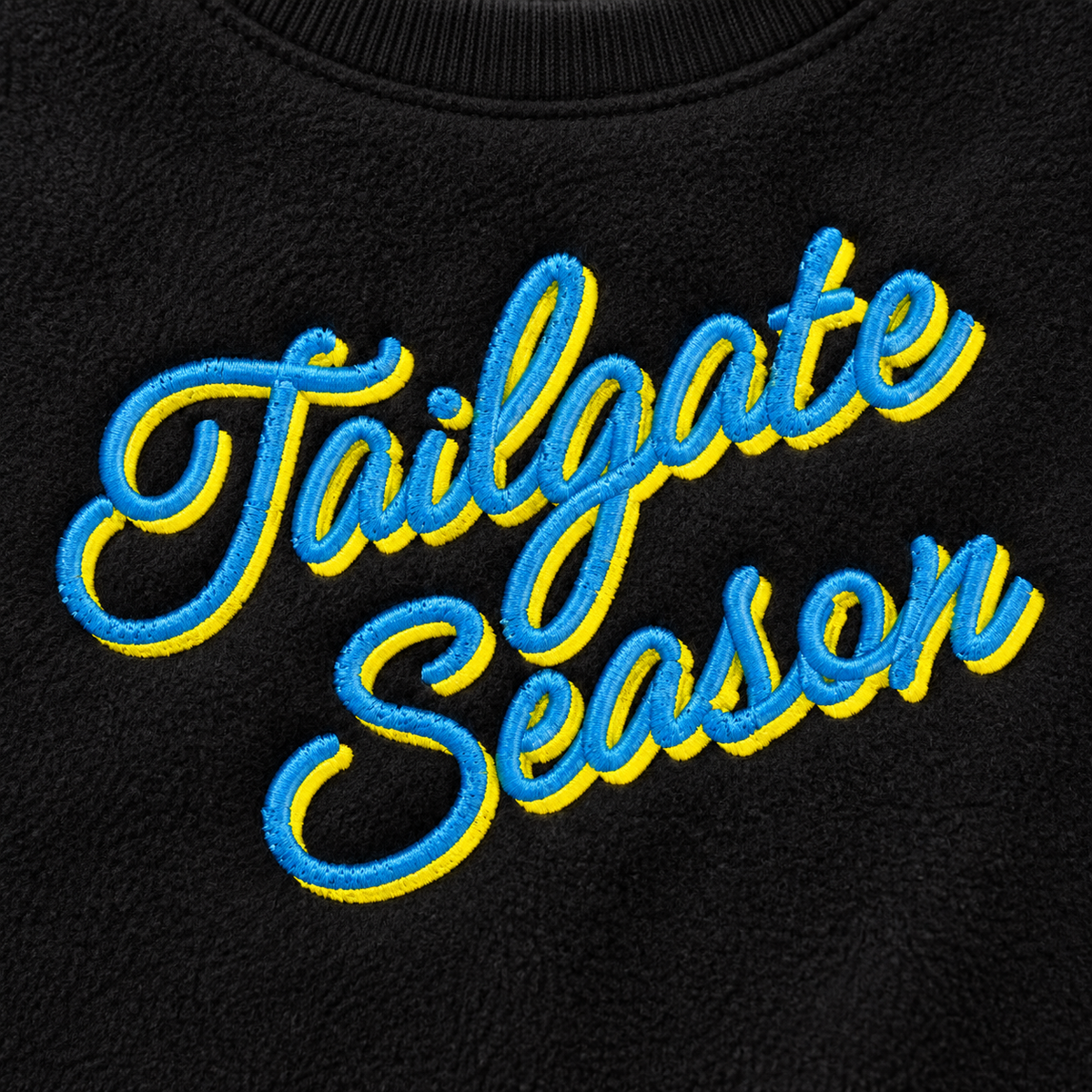 Close-up of raised blue and yellow Tailgate Season embroidery showing detailed stitching on black fleece