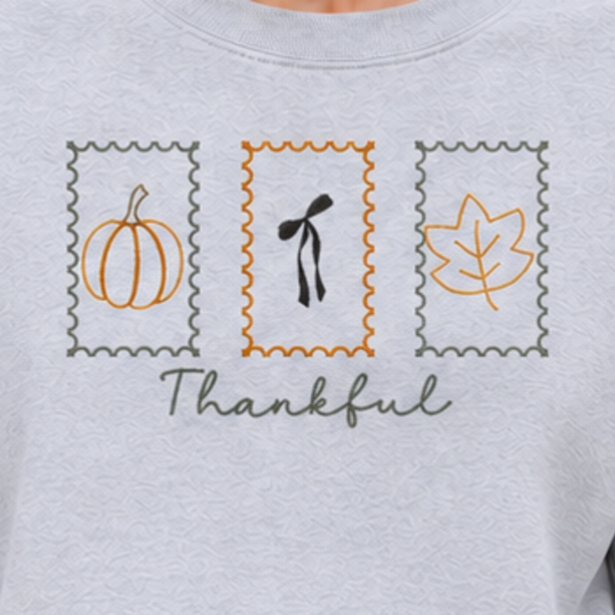 Close-up of Thankful Stamps pumpkin, bow, and leaf embroidery on Ash sweatshirt