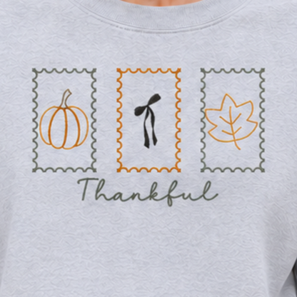 Close-up of Thankful Stamps pumpkin, bow, and leaf embroidery on Ash sweatshirt