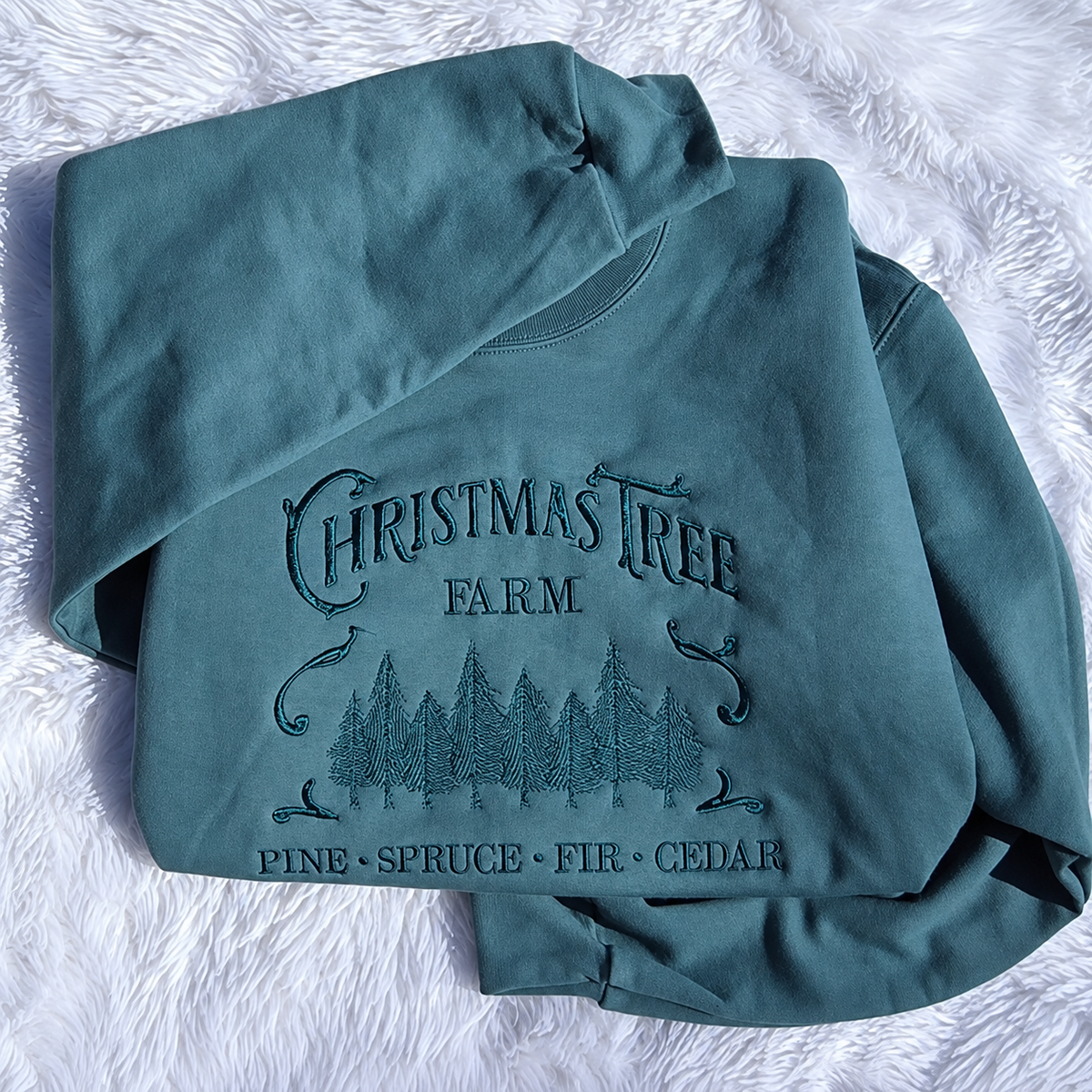 Tone-on-tone Christmas Tree Farm embroidery on a teal crewneck sweatshirt