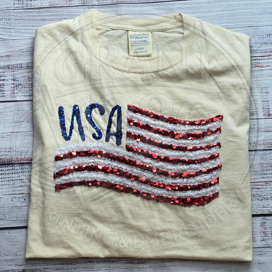 Comfort Colors ivory patriotic shirt with embroidered USA sequin lettering and waving American flag applique.