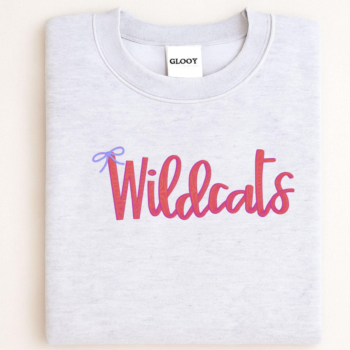 Folded ash gray crewneck with pink Wildcats script and blue bow embroidery