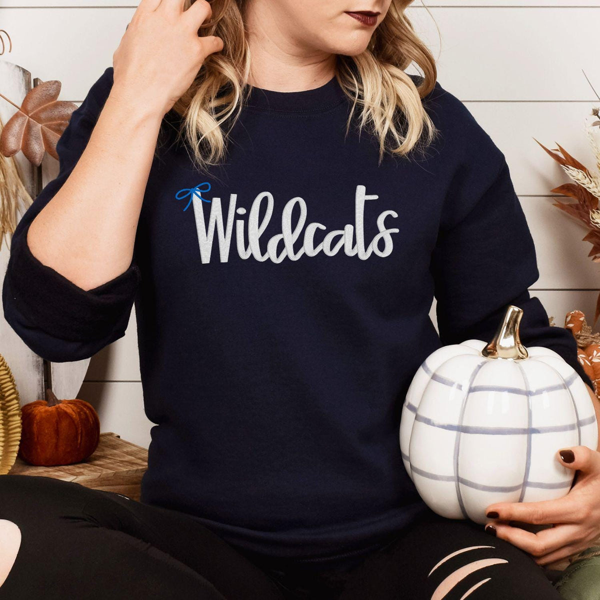 Model wearing navy Wildcats bow embroidered sweatshirt with fall pumpkins