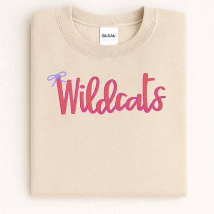 Folded sand crewneck with pink Wildcats script and blue bow embroidery