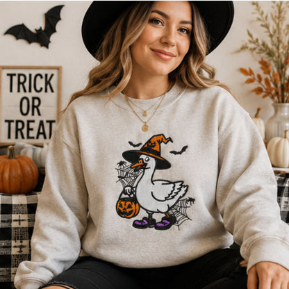 Woman in embroidered witch goose Halloween crewneck with bats, pumpkin trick-or-treat bucket and spiderwebs