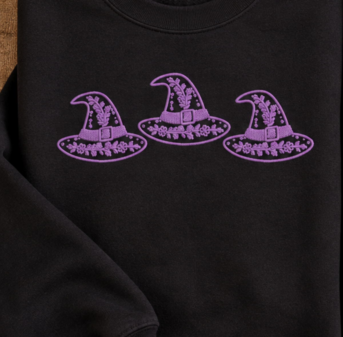 Close-up of lavender floral witch hat trio embroidery on a black sweatshirt