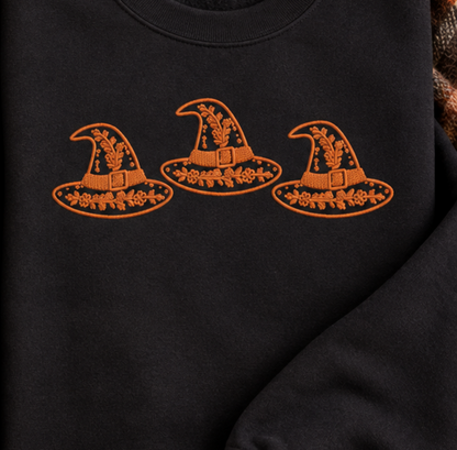 Close-up of orange floral witch hat trio embroidery on a black sweatshirt