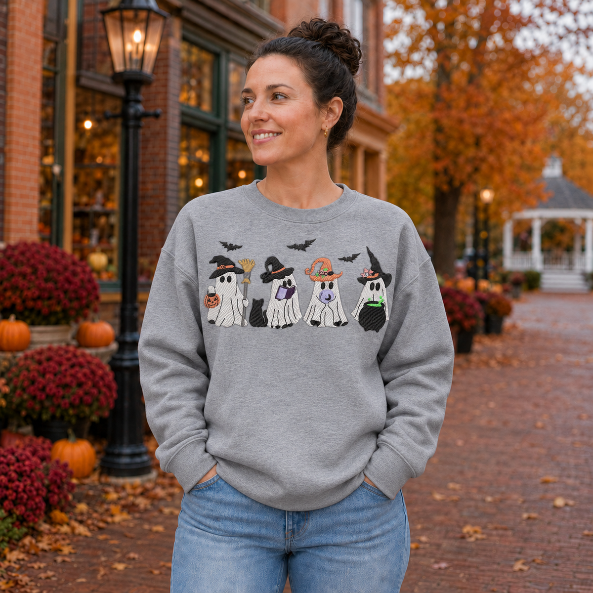 Woman wearing a Sport Grey embroidered sweatshirt with four witchy ghosts in an autumn town