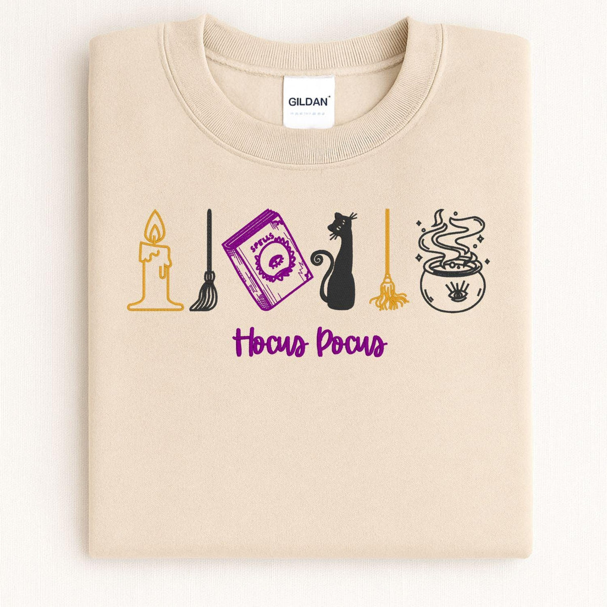 Folded Sand embroidered crewneck showing candle spell book cat broom and cauldron details